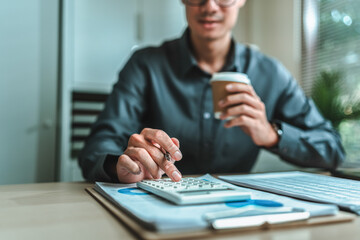 An accountant is seated at a desk in the office, utilizing a calculator to determine balances,...