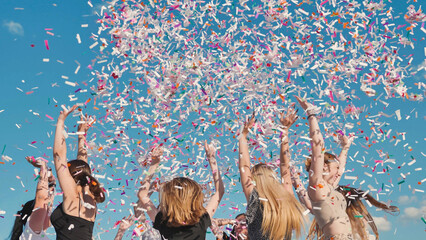 High school students celebrating graduation by throwing colorful confetti under a sunny blue sky