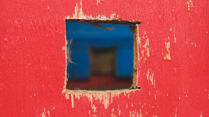 Square hole in red painted wood revealing blurred blue background