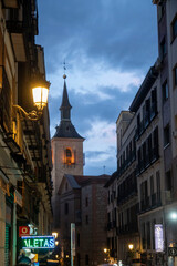A narrow street that features a clock tower prominently in the background