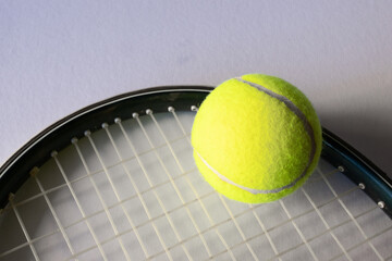 Horizontal picture of a tennis ball on a reaquet. Light background. Copy space