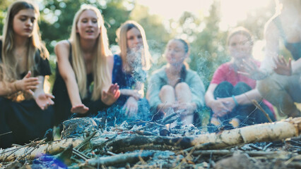 Friends huddling near campfire, sharing warmth during woodland camping adventure