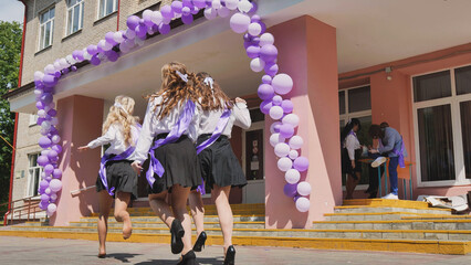 Happy graduates celebrating their last day of school, running out of the school building with...