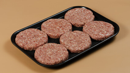 Raw burger cutlets on black tray