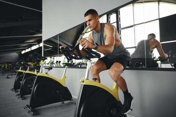 Concentrated fit man in sportswear burning calories on spin bike. Handsome athlete guy cycling on...
