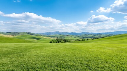 Obraz premium Lush green fields meet rolling hills under a vibrant blue sky. A picturesque landscape of springtime beauty