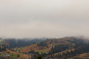 early morning in a mountain village, clouds slowly rising upwards, revealing a view of the surrounding slopes