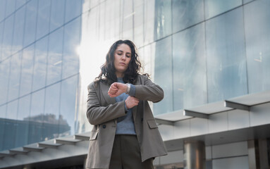 Confident woman in suit looking at her watch in front of modern glass building