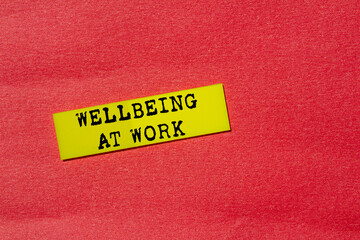 Wellbeing at work message written on yellow paper label on red background. Conceptual wellbeing at work symbol. Copy space.