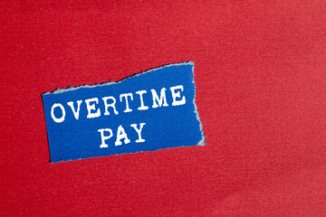 Overtime pay message written on ripped torn blue paper piece on red background. Conceptual overtime pay symbol. Copy space.
