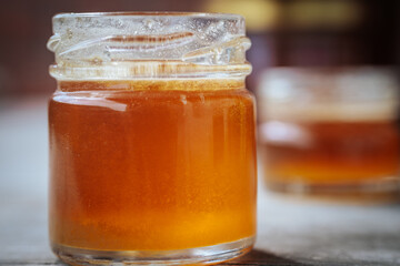 Close-up of two small glass jars filled with golden amber honey placed on a rustic wooden surface with a blurred background.
