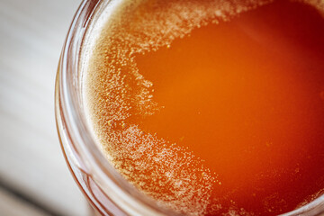 A close-up view of bubbling, fermenting honey in a glass jar on a rustic wooden surface. The bubbling texture and amber color are noticeable.
