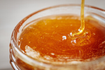 A close-up of thick golden honey being poured into a glass jar, highlighting its rich texture and natural sheen.