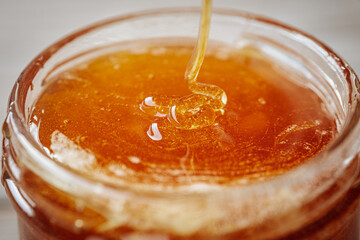 A close-up of thick golden honey being poured into a glass jar, highlighting its rich texture and natural sheen.