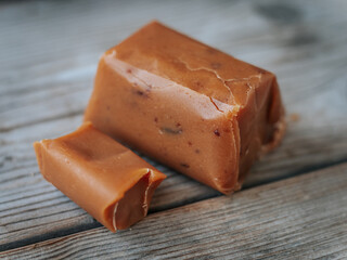 Close-up of two caramel candy pieces, one whole and one cut, displayed on a rustic wooden background with soft focus in the back.