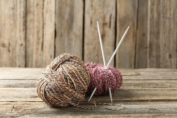 Skeins of colorful yarn and knitting needles on wooden table, closeup