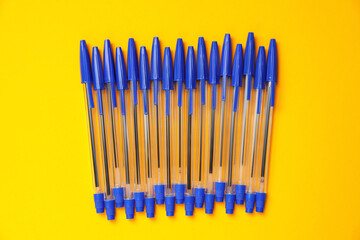 Many ballpoint pens with caps on orange background, flat lay