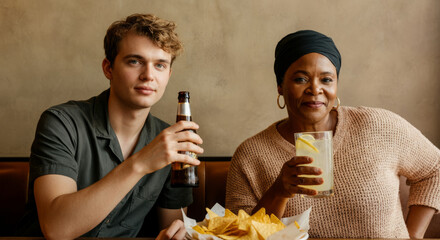 Young caucasian male and mature african female sharing drinks at a table with nachos