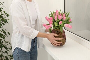 Fototapeta premium Woman arranging vase with bouquet of beautiful tulips onto window sill indoors, closeup