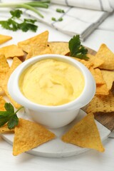 Tasty dipping cheese sauce in bowl and nacho chips on white wooden table, closeup