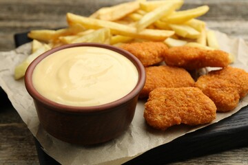 Delicious cheese sauce in bowl, chicken nuggets and French fries on wooden table, closeup