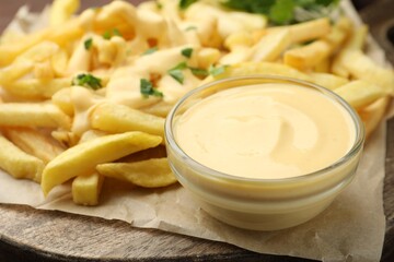 Delicious cheese sauce in bowl, French fries and parsley on table, closeup
