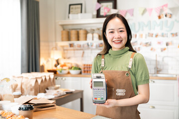 Smiling cashier woman offering credit card payment machine to customer in small bakery shop representing convenient service and modern cashless transaction in friendly business environment