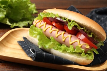 Tasty hot dog with tomato, onion, lettuce and mustard on wooden table, closeup