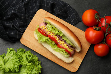 Tasty hot dog with vegetables on black table, flat lay
