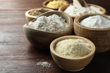 Different types of flour in bowls on wooden table, closeup