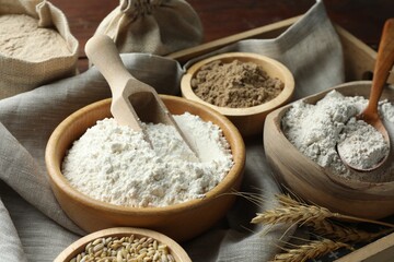 Different types of flour in bowls on wooden table, closeup
