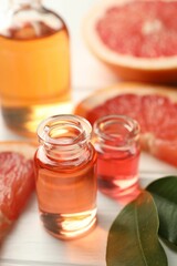 Open perfume bottles with aromatic essential oils, leaves and slices of grapefruit on white wooden table, closeup