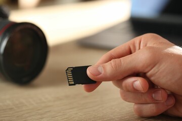 Man with SD memory card at wooden table indoors, closeup