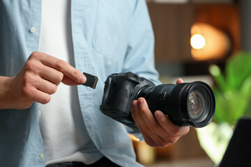 Man inserting SD memory card into photo camera indoors, closeup