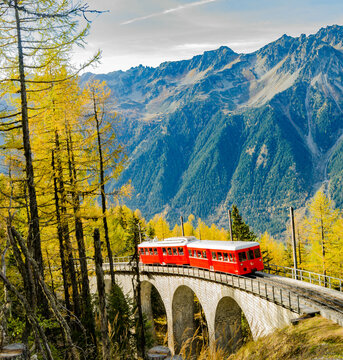 Train rouge traversant un pont en pierre dans les Alpes en automne