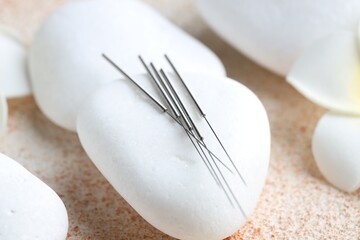 Acupuncture needles and spa stones on light textured table, closeup