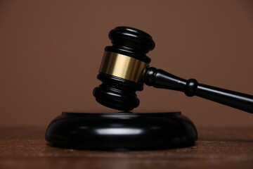 Judge's gavel and sound block on wooden table against brown background, closeup