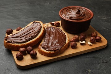 Toasts with tasty chocolate hazelnut spread and nuts on black table