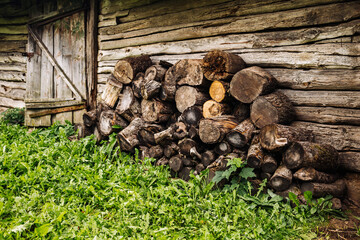 Firewood stacked near old barn in countryside with green grass