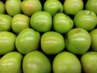 A clean layout of green apples arranged closely, with their glossy skin and natural blemishes creating an appealing, healthy, and natural fruit texture.