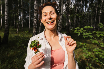 Woman eating wild strawberry sitting on grass in summer forest. Female enjoying nature, healthy...