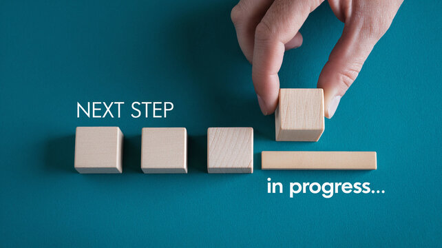 Hand placing wooden block, symbolizing next step in progress, on teal background Four blocks represent stages, showcasing business growth concept