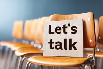 A sign reading "Let's talk" sits on an empty wooden chair in a row of similar chairs, suggesting an invitation for conversation.
