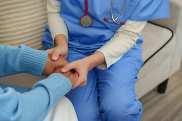 Asian female physical therapist wearing blue uniform holding elderly male patient's hand gently...