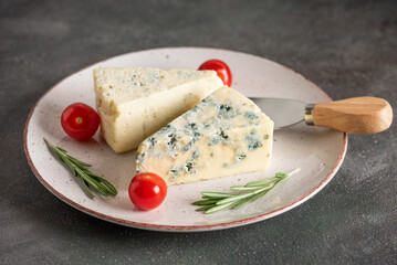 Blue cheese on a plate with a cheese knife, rosemary and cherry tomatoes, selective focus, dark rustic background