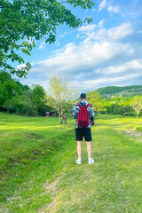 A young man is a traveler with a red backpack, relaxing in the fresh air against the backdrop of mountains, summer holidays and the concept of a hiking lifestyle