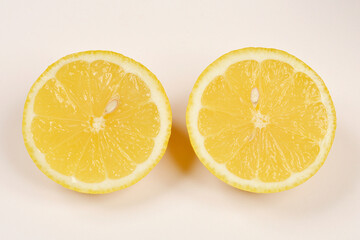 Two halves of a bright yellow lemon are positioned side-by-side on a light surface, showcasing...