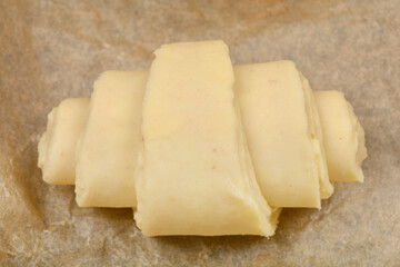 A single, unbaked croissant dough rests on a piece of parchment paper, ready for the oven