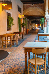 Cozy outdoor cafe with wooden tables and chairs outside under historic archways in old town of Verona city, Veneto, Italy. Italian vintage style sidewalk restaurant in narrow cobblestone alley