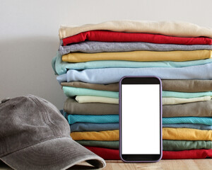 Stack of colorful clothes with a smartphone and a cap displaying online shopping concept